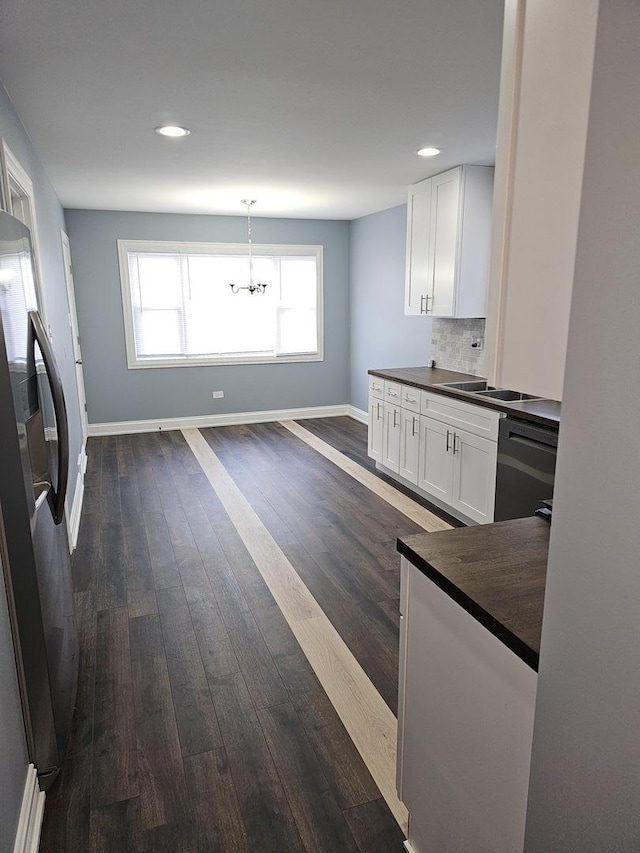 kitchen featuring dark countertops, dark wood finished floors, black dishwasher, freestanding refrigerator, and white cabinetry