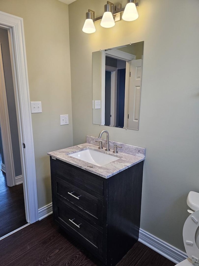 half bath with baseboards, toilet, wood finished floors, and vanity