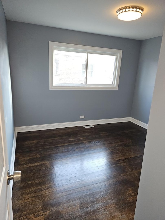 spare room with visible vents, baseboards, and dark wood-style flooring