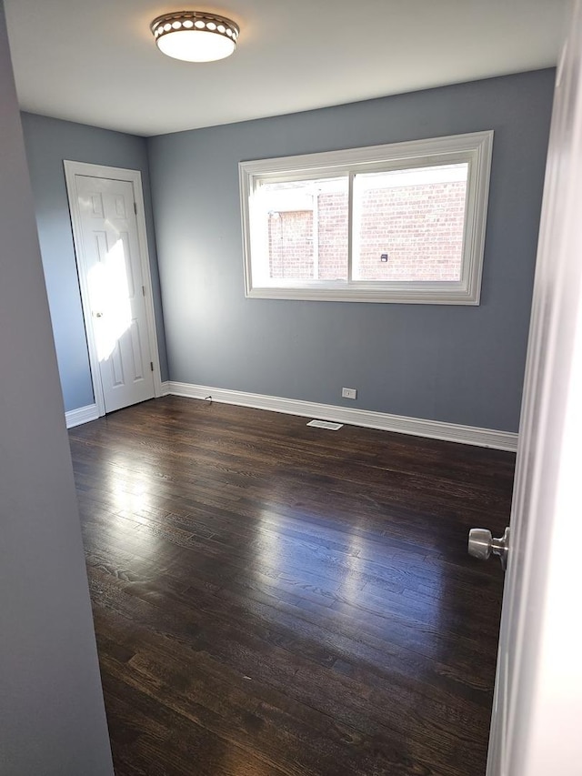 empty room featuring dark wood-style floors, visible vents, and baseboards