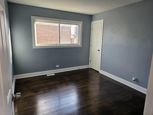 spare room featuring dark wood finished floors, visible vents, and baseboards