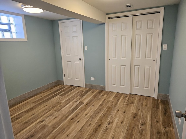 unfurnished bedroom featuring wood finished floors, visible vents, a closet, and baseboards