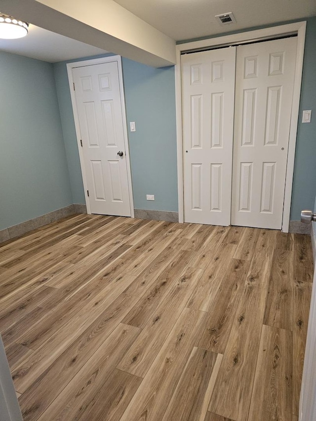 unfurnished bedroom with a closet, visible vents, baseboards, and wood finished floors