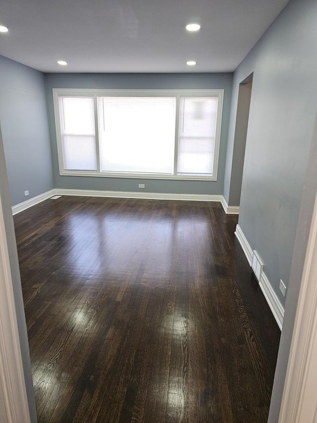 spare room with dark wood-style floors, visible vents, baseboards, and a wealth of natural light