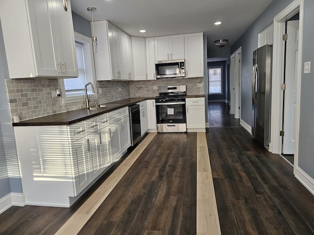 kitchen featuring dark wood-style floors, a sink, white cabinets, appliances with stainless steel finishes, and dark countertops