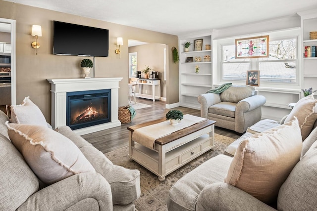 living room with a glass covered fireplace, wood finished floors, and baseboards