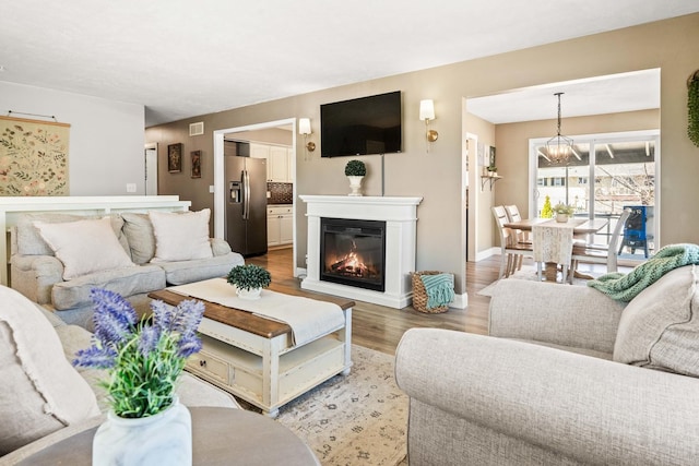 living area with a glass covered fireplace, visible vents, light wood-type flooring, and baseboards