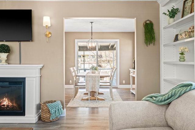 living room with built in shelves, baseboards, an inviting chandelier, wood finished floors, and a glass covered fireplace