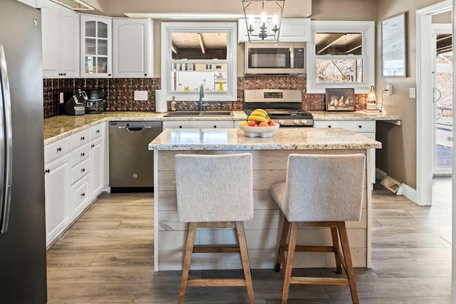 kitchen with a sink, tasteful backsplash, light wood-style floors, appliances with stainless steel finishes, and white cabinets