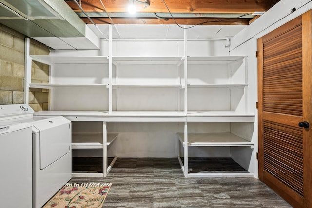 clothes washing area featuring dark wood-style floors, laundry area, concrete block wall, and washing machine and clothes dryer