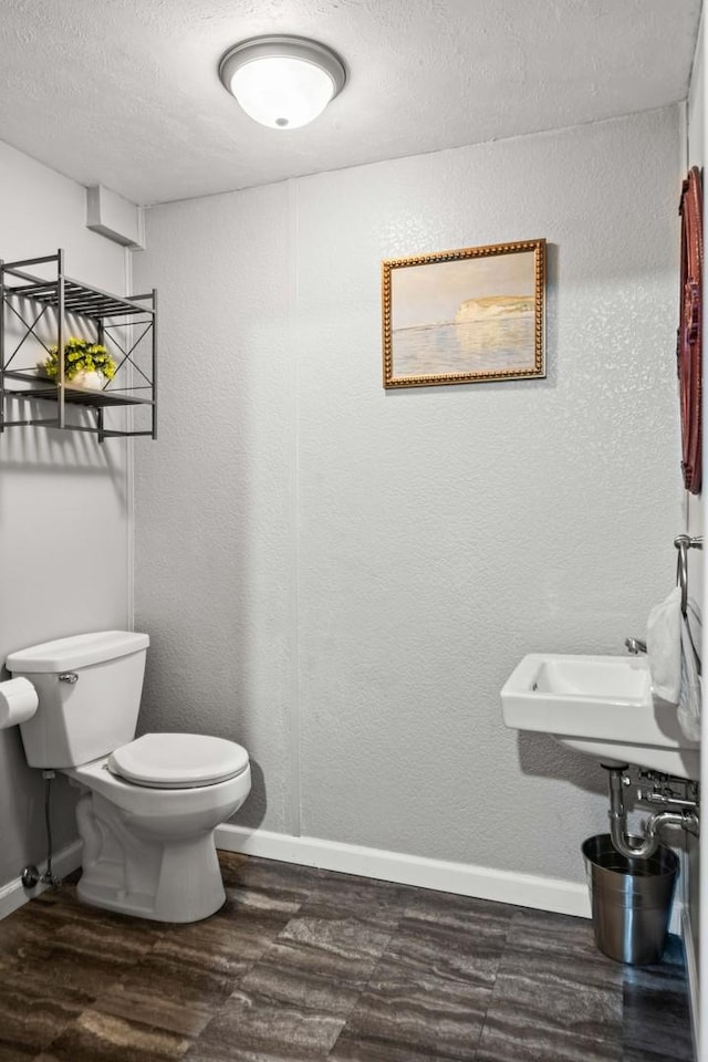 bathroom featuring a textured wall, toilet, baseboards, and wood finished floors