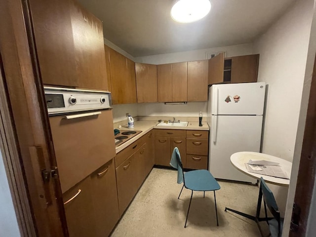 kitchen featuring wall oven, light countertops, electric cooktop, freestanding refrigerator, and a sink