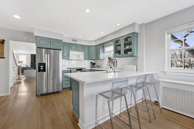 kitchen featuring white microwave, a healthy amount of sunlight, radiator, stainless steel fridge with ice dispenser, and a peninsula