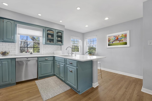 kitchen with light wood-style flooring, a sink, a peninsula, decorative backsplash, and dishwasher