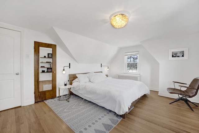 bedroom with light wood-style flooring, radiator heating unit, and vaulted ceiling