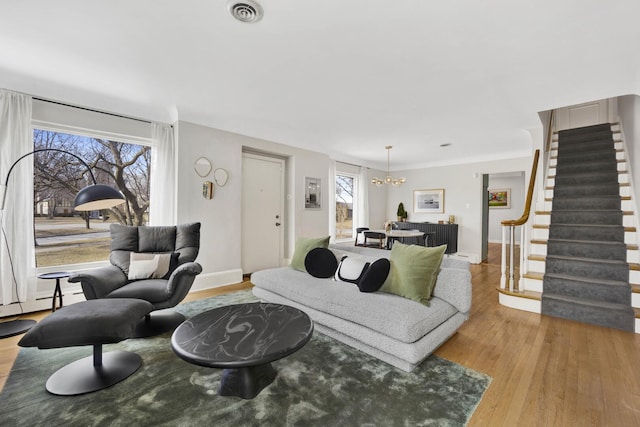 living area featuring baseboards, visible vents, light wood-style flooring, stairs, and a notable chandelier