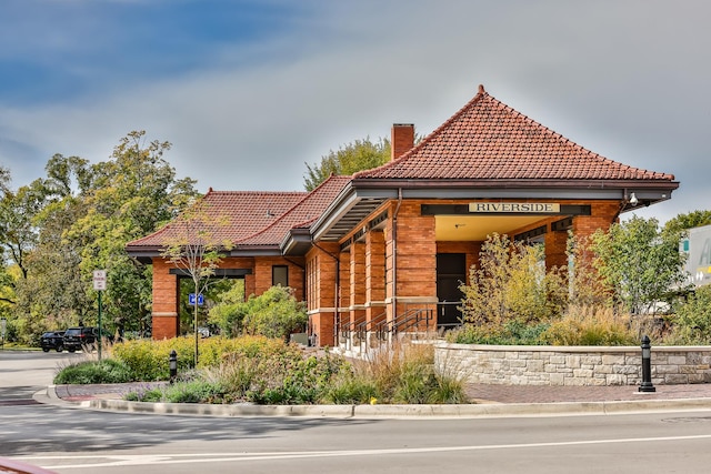 view of front of property featuring brick siding, a chimney, and a tiled roof