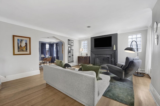 living area featuring wood finished floors, baseboards, a fireplace, arched walkways, and a baseboard heating unit