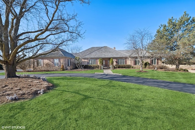 ranch-style house with brick siding, a chimney, and a front yard