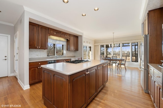 kitchen with a kitchen island, light wood-style flooring, ornamental molding, stainless steel appliances, and light countertops