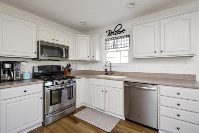 kitchen with dark wood-type flooring, white cabinets, appliances with stainless steel finishes, and a sink