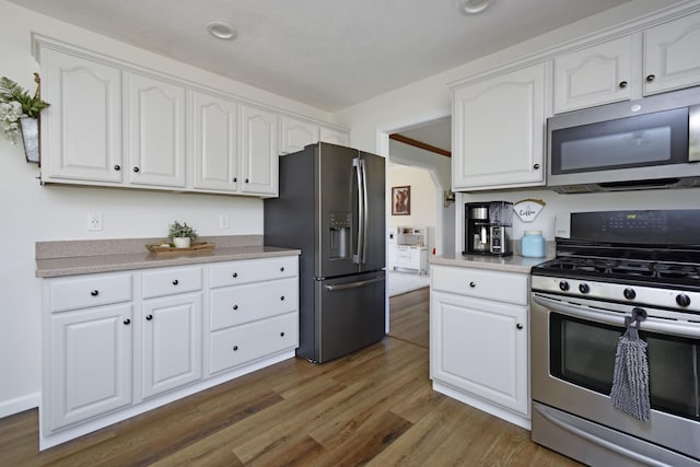 kitchen with white cabinets, appliances with stainless steel finishes, light countertops, and wood finished floors