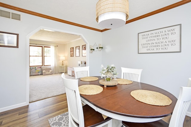 dining room featuring wood finished floors, visible vents, baseboards, arched walkways, and crown molding