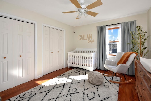 bedroom with a ceiling fan, a nursery area, wood finished floors, and two closets