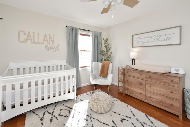 bedroom with a crib, wood finished floors, baseboards, and ceiling fan