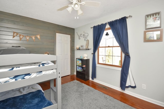 bedroom featuring wood finished floors, baseboards, visible vents, ceiling fan, and a textured ceiling