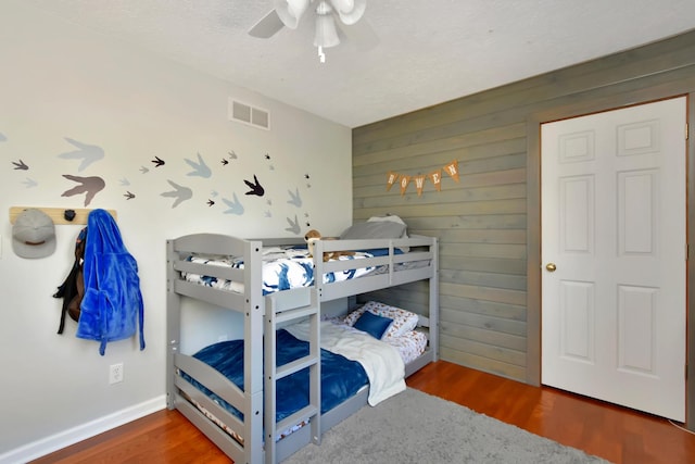 bedroom with visible vents, wooden walls, and wood finished floors