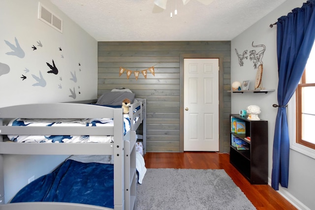 bedroom with visible vents, a textured ceiling, wood finished floors, and wood walls