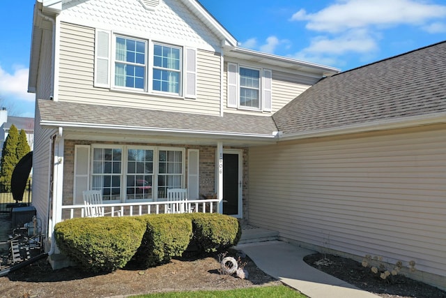 entrance to property featuring a porch and a shingled roof