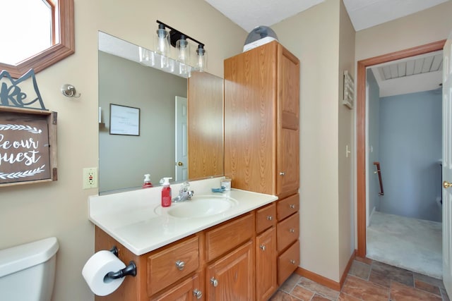 bathroom with baseboards, toilet, vanity, and stone finish floor