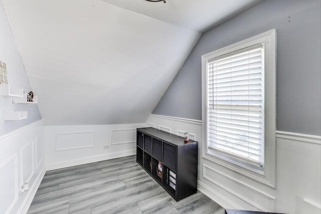 additional living space featuring a decorative wall, light wood-type flooring, and vaulted ceiling