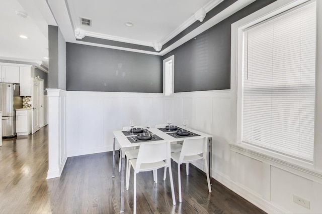 dining space with visible vents, wainscoting, a decorative wall, crown molding, and dark wood-style flooring