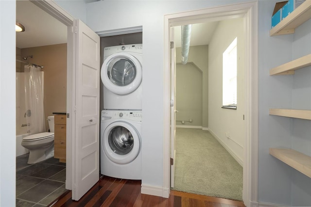 laundry area with dark wood finished floors, laundry area, stacked washer and dryer, and baseboards