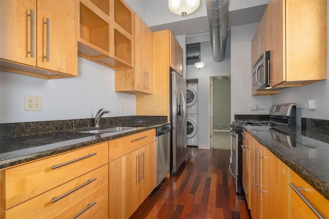 kitchen with dark stone countertops, dark wood finished floors, a sink, stainless steel appliances, and stacked washer / drying machine