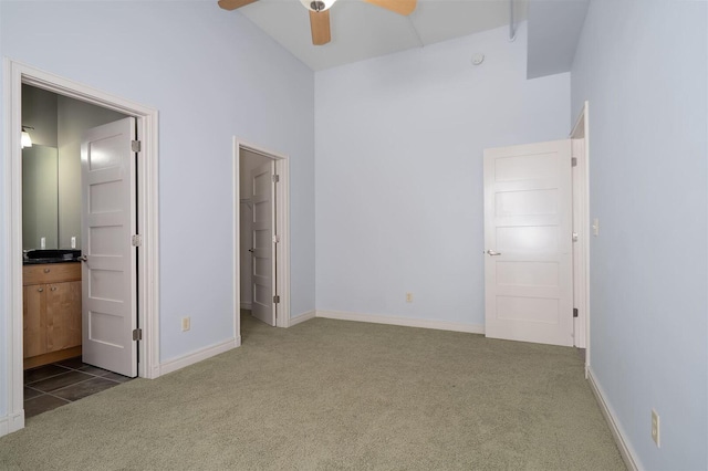 unfurnished bedroom featuring baseboards, carpet floors, ensuite bathroom, high vaulted ceiling, and a ceiling fan