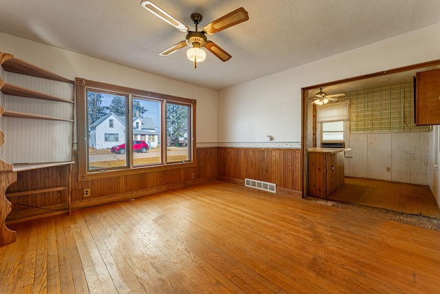 spare room featuring hardwood / wood-style floors, a ceiling fan, visible vents, wainscoting, and a textured ceiling