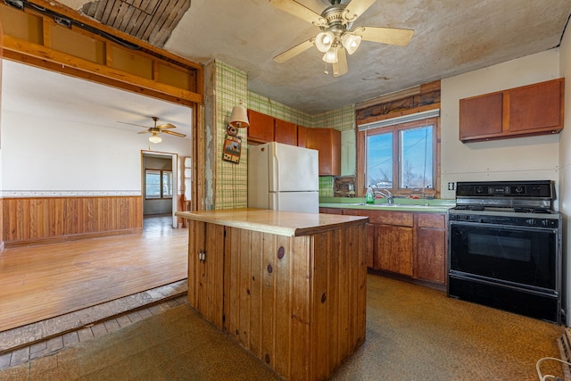 kitchen featuring black gas range, a healthy amount of sunlight, wainscoting, and freestanding refrigerator