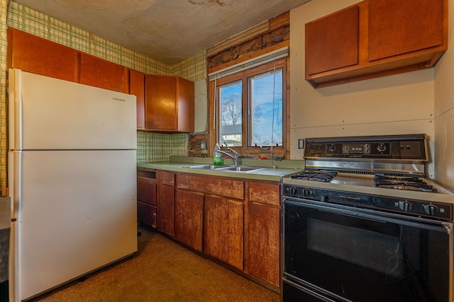 kitchen featuring a sink, range with gas stovetop, light countertops, and freestanding refrigerator