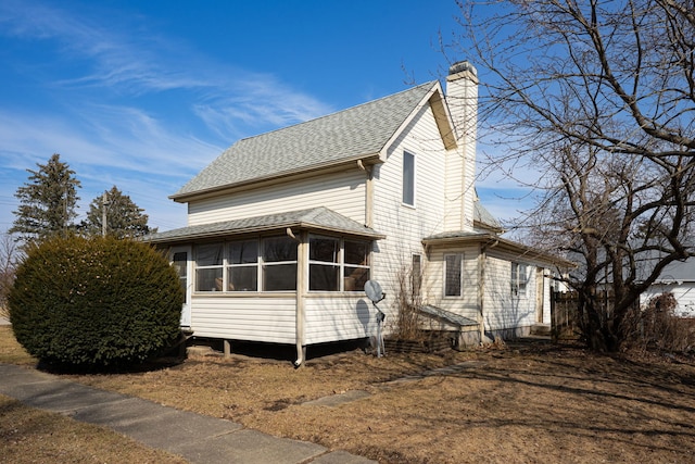 view of side of property with roof with shingles, a chimney, and a sunroom