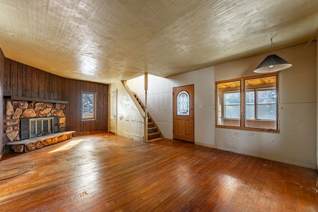 unfurnished living room featuring a stone fireplace, a healthy amount of sunlight, stairs, and hardwood / wood-style floors