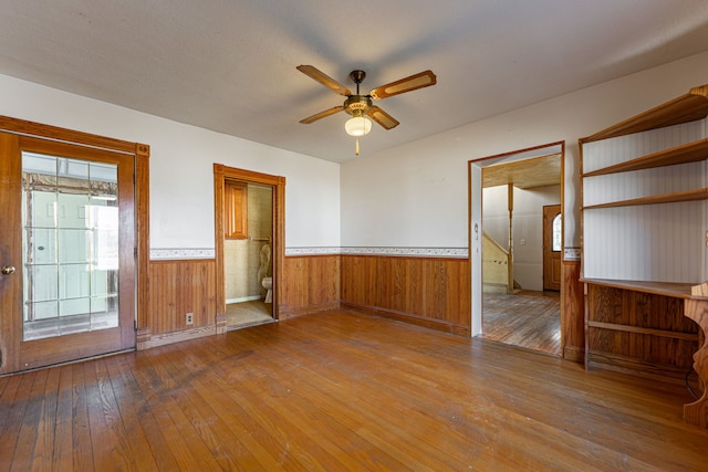 spare room featuring hardwood / wood-style flooring, a wainscoted wall, wood walls, and ceiling fan