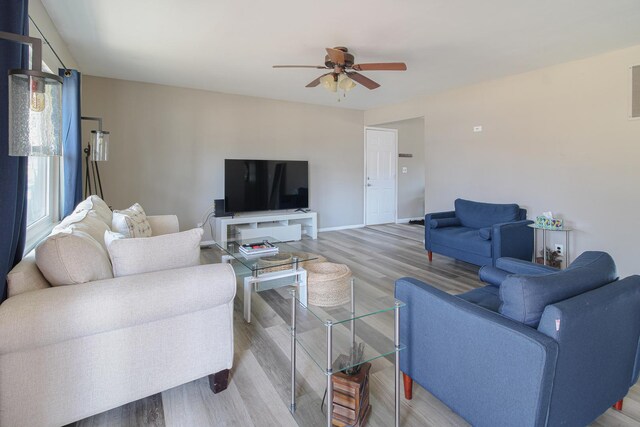 living area with baseboards, light wood-style floors, and a ceiling fan