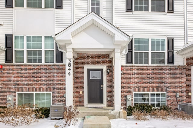 snow covered property entrance featuring central air condition unit and brick siding