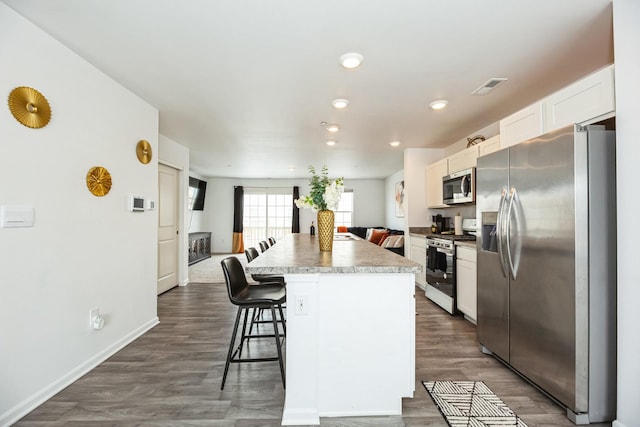 kitchen featuring a kitchen bar, dark wood-type flooring, a kitchen island, white cabinetry, and stainless steel appliances