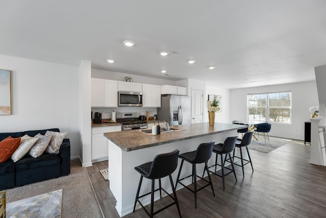 kitchen with open floor plan, an island with sink, appliances with stainless steel finishes, a kitchen breakfast bar, and a sink