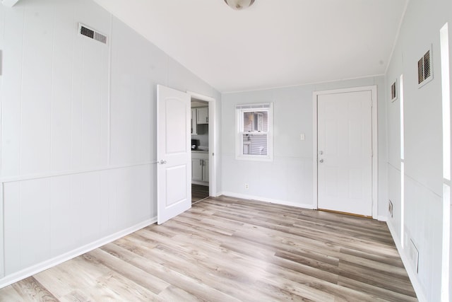 unfurnished room featuring visible vents, light wood-style floors, and vaulted ceiling